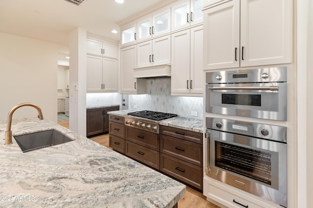 kitchen with dark brown cabinetry, white cabinetry, sink, and light stone countertops