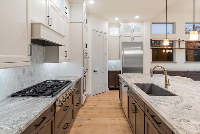 kitchen with light wood-type flooring, stainless steel appliances, sink, decorative light fixtures, and white cabinets