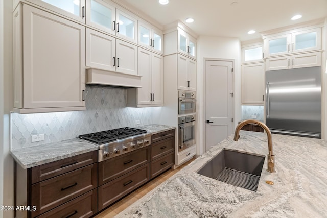 kitchen featuring appliances with stainless steel finishes, dark brown cabinetry, custom exhaust hood, and sink