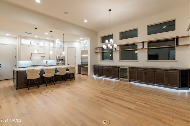 kitchen with hanging light fixtures, appliances with stainless steel finishes, light hardwood / wood-style floors, white cabinetry, and beverage cooler