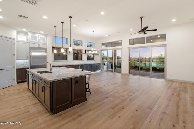 kitchen with a kitchen island with sink, ceiling fan with notable chandelier, sink, light wood-type flooring, and stainless steel built in refrigerator