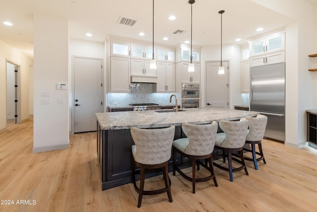 kitchen with a center island with sink, sink, light hardwood / wood-style floors, white cabinetry, and stainless steel appliances