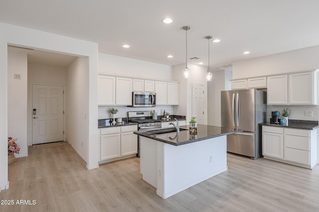 kitchen featuring appliances with stainless steel finishes, decorative light fixtures, light hardwood / wood-style flooring, white cabinets, and an island with sink