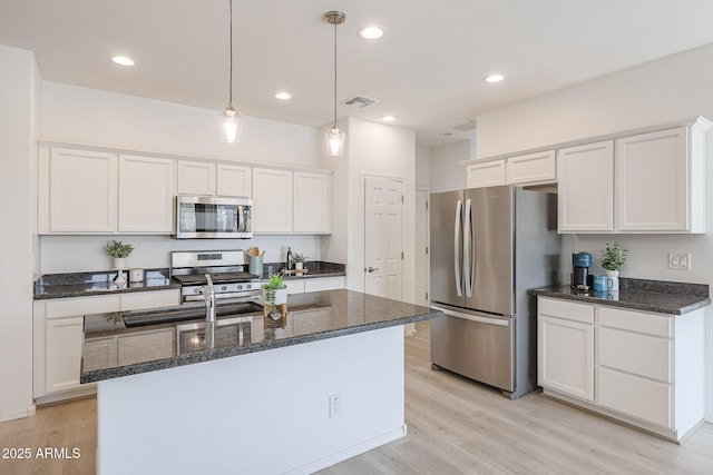 kitchen with hanging light fixtures, an island with sink, appliances with stainless steel finishes, light hardwood / wood-style floors, and white cabinetry