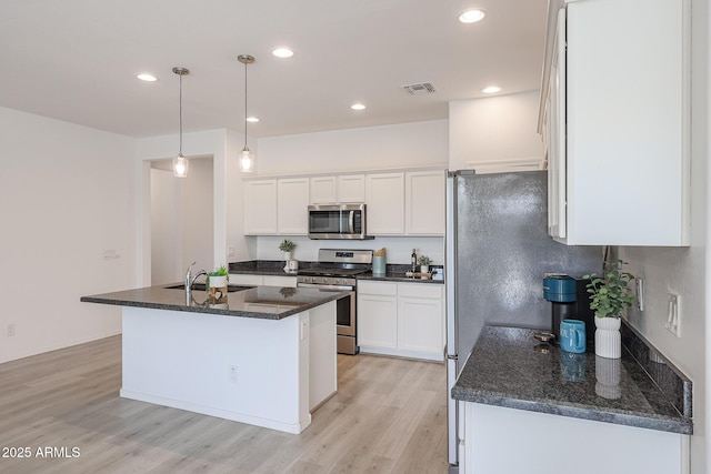 kitchen with stainless steel appliances, a kitchen island with sink, sink, pendant lighting, and white cabinets