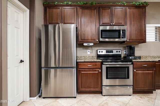 kitchen featuring light tile patterned floors, light stone countertops, dark brown cabinetry, and stainless steel appliances