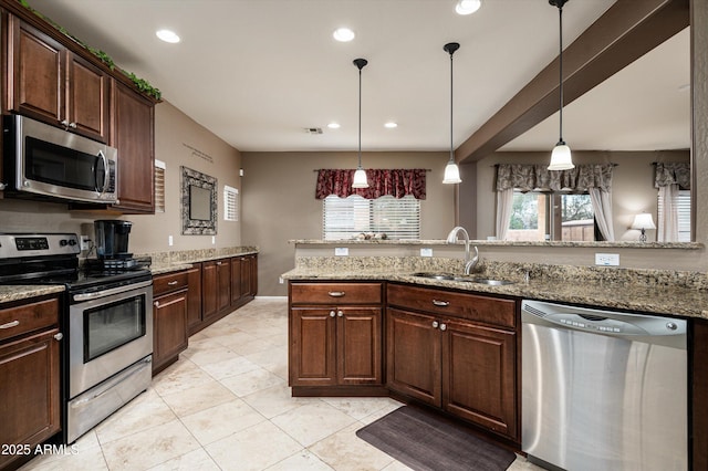 kitchen featuring light stone countertops, dark brown cabinetry, appliances with stainless steel finishes, sink, and hanging light fixtures