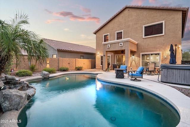 pool at dusk featuring a patio area and a hot tub