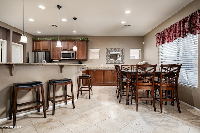 kitchen with stainless steel appliances, decorative light fixtures, light stone countertops, a breakfast bar, and a center island