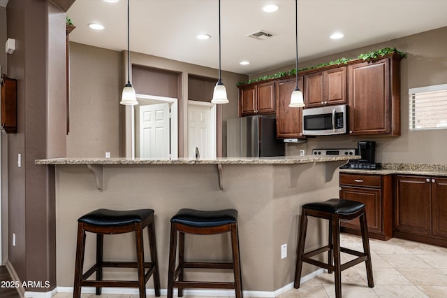 kitchen featuring a kitchen bar, light tile patterned flooring, hanging light fixtures, appliances with stainless steel finishes, and light stone counters