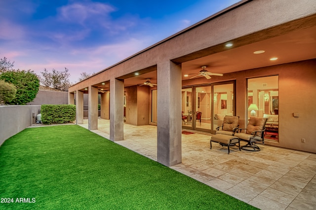 patio terrace at dusk featuring ceiling fan and a yard