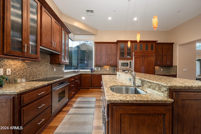 kitchen with built in appliances, sink, hanging light fixtures, and an island with sink