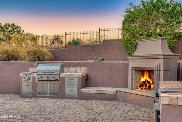 patio terrace at dusk featuring area for grilling, exterior fireplace, and a grill