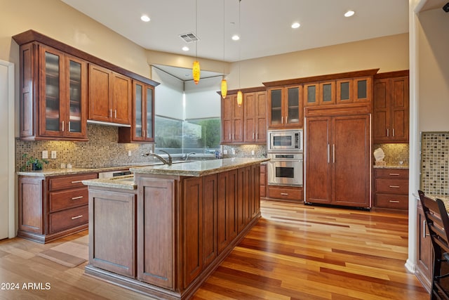 kitchen with light stone counters, built in appliances, pendant lighting, light hardwood / wood-style floors, and a kitchen island