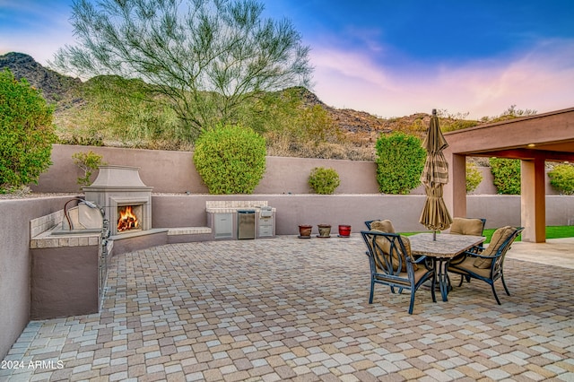 patio terrace at dusk featuring a mountain view, area for grilling, and exterior fireplace