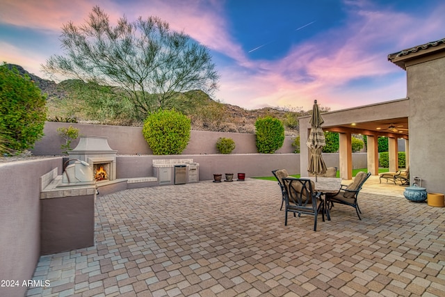 patio terrace at dusk with a mountain view and an outdoor fireplace