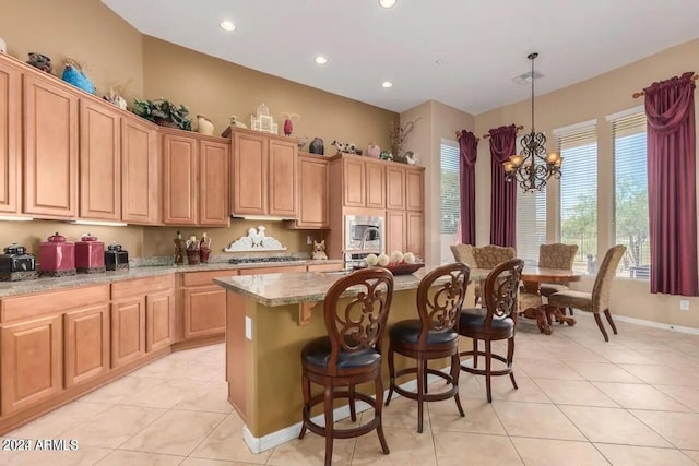 kitchen with light stone counters, light tile patterned floors, a kitchen island, decorative light fixtures, and an inviting chandelier