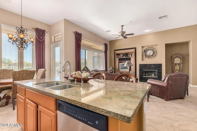 kitchen with sink, a center island with sink, dishwasher, a tile fireplace, and light stone countertops