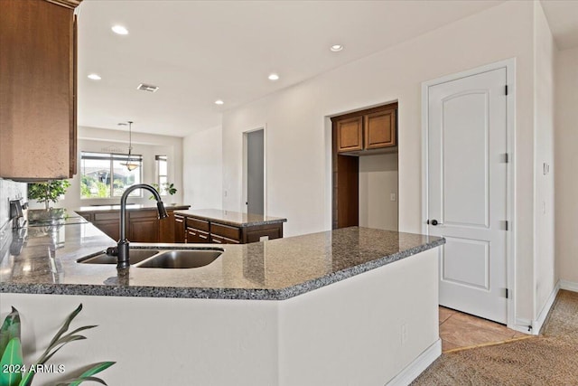 kitchen featuring kitchen peninsula, sink, hanging light fixtures, and dark stone counters