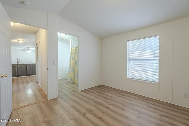 empty room with lofted ceiling, sink, ceiling fan, and light hardwood / wood-style flooring