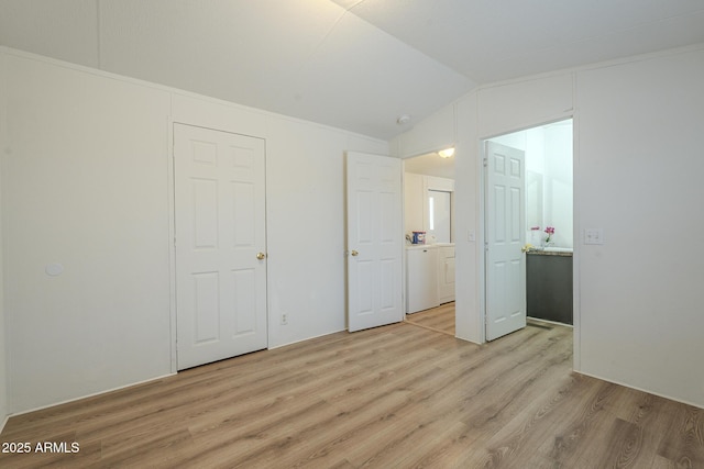 unfurnished bedroom with lofted ceiling, washer / dryer, and light hardwood / wood-style floors