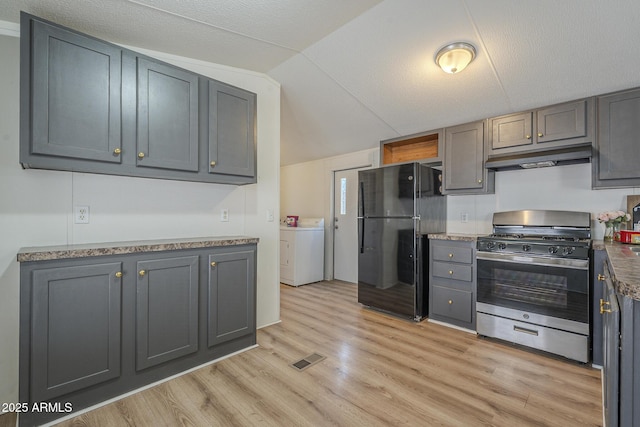 kitchen with black fridge, stainless steel gas stove, lofted ceiling, washer / dryer, and gray cabinetry