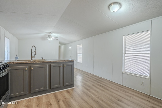 kitchen with sink, stainless steel stove, vaulted ceiling, ceiling fan, and light wood-type flooring