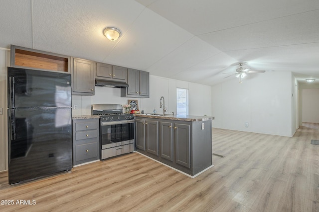 kitchen with kitchen peninsula, stainless steel gas range, black fridge, light hardwood / wood-style floors, and sink