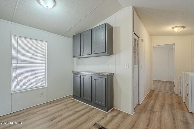 interior space featuring gray cabinetry, light wood-type flooring, lofted ceiling, and washer and dryer