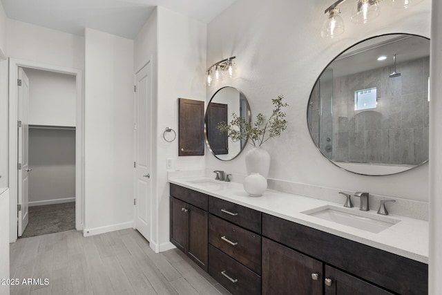 bathroom with double vanity, wood finished floors, a sink, and tiled shower