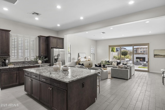 kitchen with stainless steel refrigerator with ice dispenser, a sink, dark brown cabinetry, light wood-type flooring, and a lit fireplace