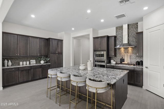 kitchen featuring visible vents, a kitchen island, a kitchen breakfast bar, stainless steel appliances, and wall chimney range hood