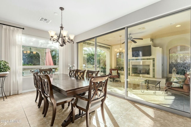 dining area with a tile fireplace, light tile patterned floors, and ceiling fan with notable chandelier