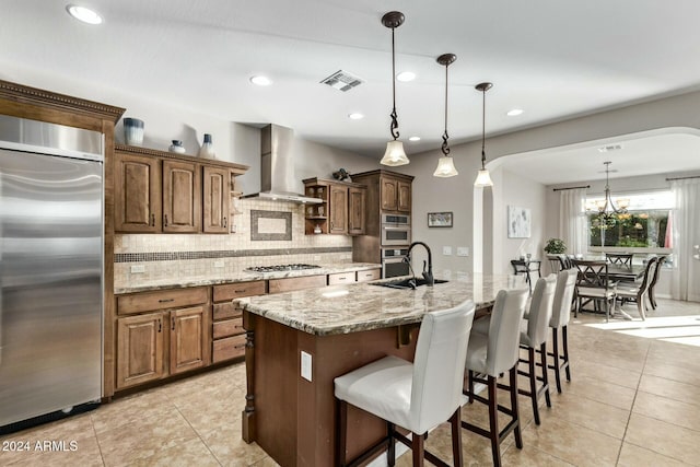 kitchen with light stone countertops, wall chimney exhaust hood, stainless steel appliances, a spacious island, and pendant lighting