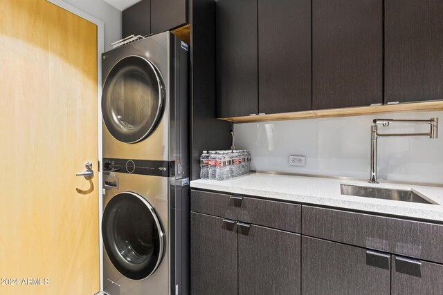 clothes washing area featuring cabinets, stacked washing maching and dryer, and sink