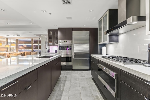 kitchen with appliances with stainless steel finishes, light stone counters, wall chimney exhaust hood, dark brown cabinetry, and sink