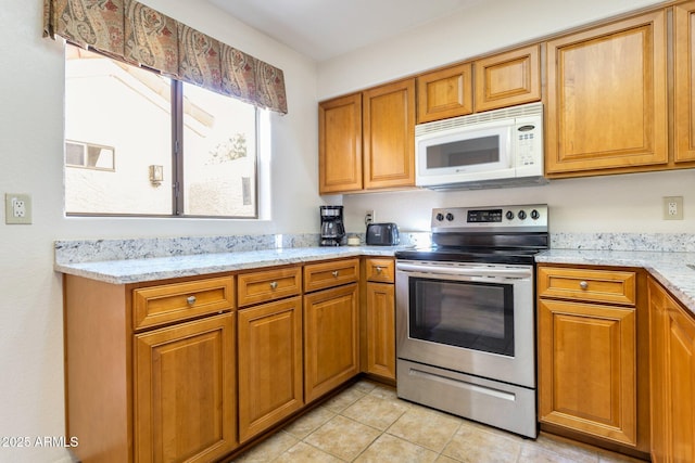 kitchen with stainless steel electric stove, light stone counters, and light tile patterned flooring