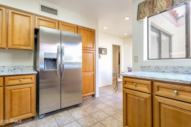 kitchen with light stone counters, light tile patterned floors, and stainless steel fridge