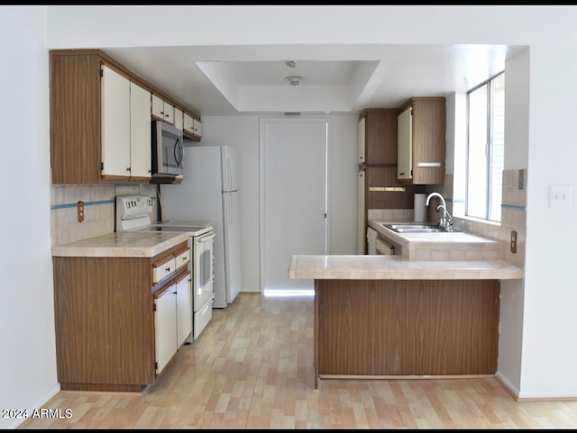 kitchen featuring a raised ceiling, sink, light hardwood / wood-style flooring, white range with electric stovetop, and kitchen peninsula