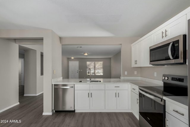 kitchen with a peninsula, a sink, white cabinets, light countertops, and appliances with stainless steel finishes