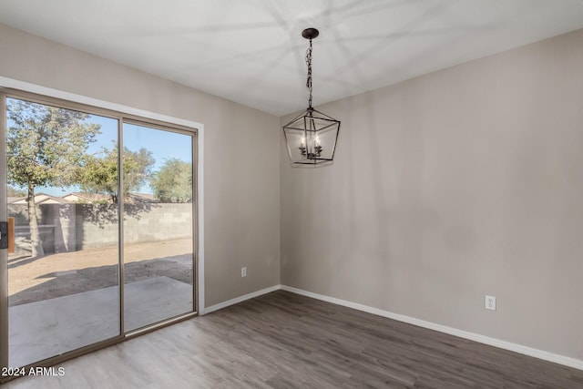 unfurnished dining area featuring a notable chandelier, wood finished floors, and baseboards