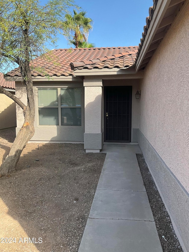 view of exterior entry with a tile roof and stucco siding