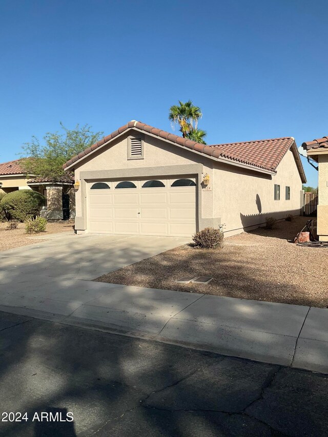 exterior space with driveway, central AC unit, a tile roof, an attached garage, and stucco siding