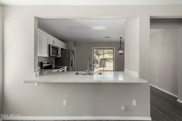 kitchen with light stone counters, a peninsula, a sink, white cabinets, and appliances with stainless steel finishes