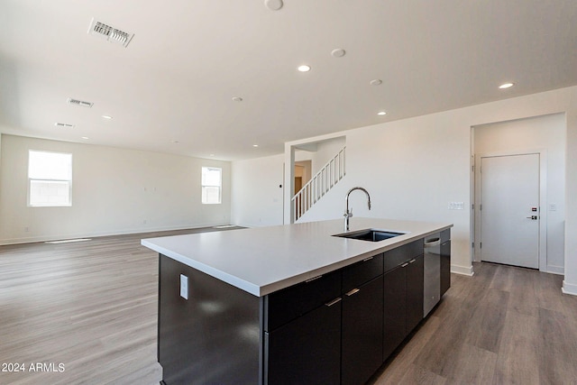 kitchen with sink, dishwasher, a kitchen island with sink, and light wood-type flooring