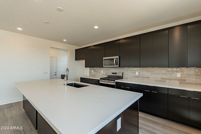 kitchen with light wood-type flooring, sink, a center island with sink, and appliances with stainless steel finishes