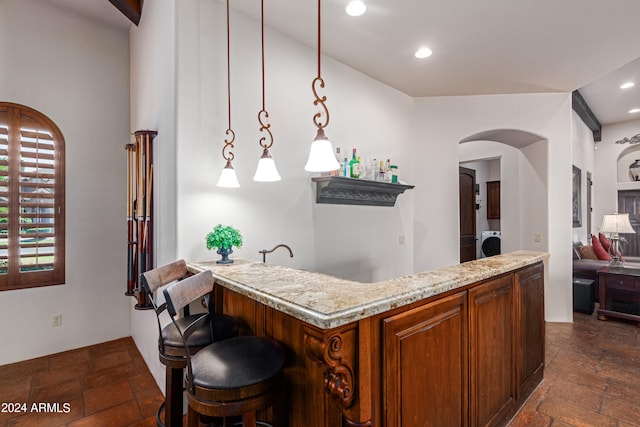 kitchen featuring decorative light fixtures, a kitchen breakfast bar, light stone counters, and washer / clothes dryer