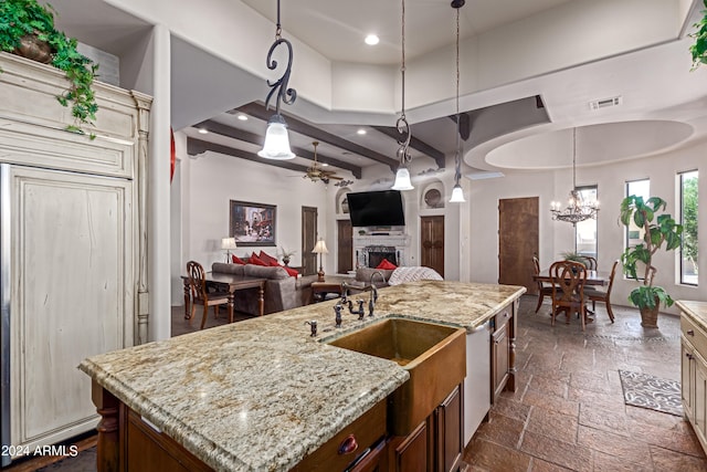 kitchen with dishwasher, light stone counters, an island with sink, decorative light fixtures, and ceiling fan with notable chandelier