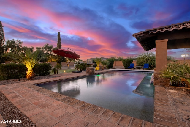 pool at dusk featuring pool water feature and a patio area