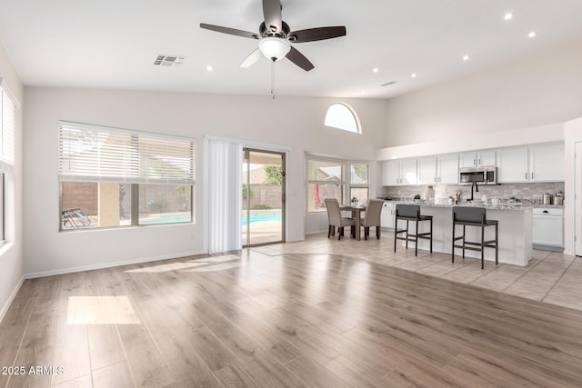 unfurnished living room featuring visible vents, high vaulted ceiling, a ceiling fan, light wood finished floors, and baseboards